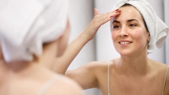 Mujer aplicándose crema frente al espejo.